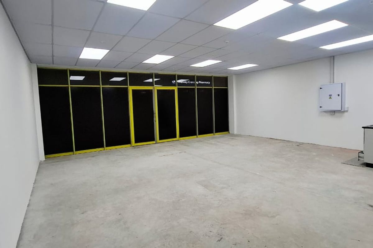An open-plan commercial space featuring a suspended ceiling, recessed lighting, large glass storefront, and a small kitchenette area, suitable for retail or office use.