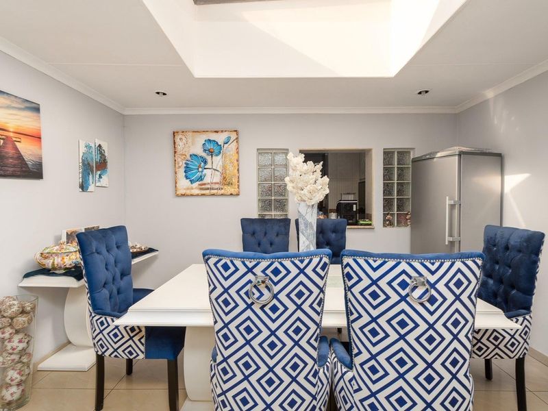 A bright dining room featuring a large central skylight, tiled flooring, and a pass-through window connecting to the kitchen area.
