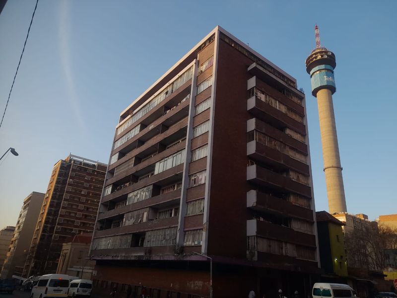 Exterior view of a multi-story brick apartment building featuring multiple balconies and large windows, situated in an urban environment.