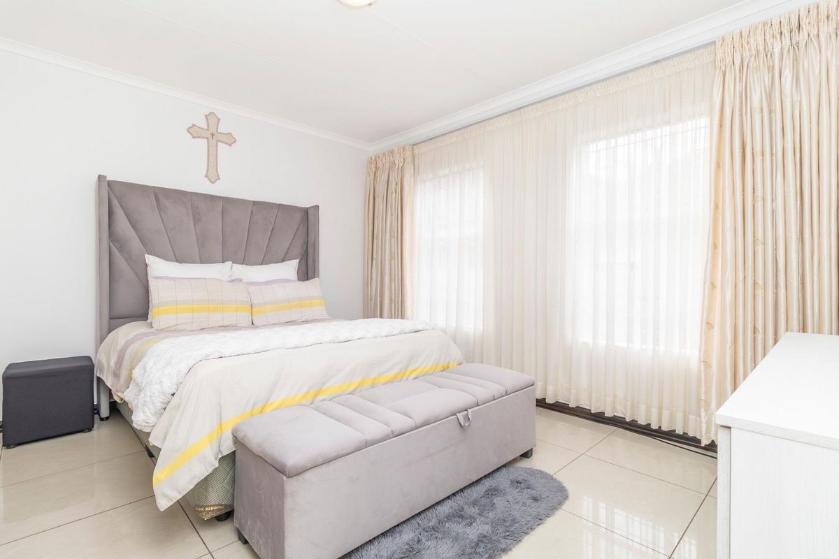 A bright and well-maintained bedroom featuring large windows with floor-to-ceiling curtains and neutral tiled flooring.
