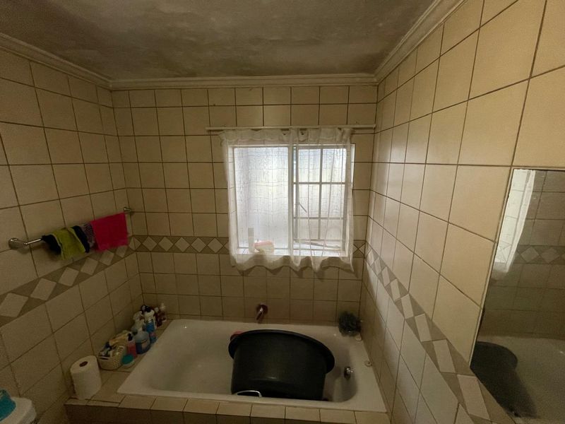 A dated bathroom featuring a built-in bathtub with tiled walls and a window, requiring cosmetic updates to improve its overall condition and appeal.