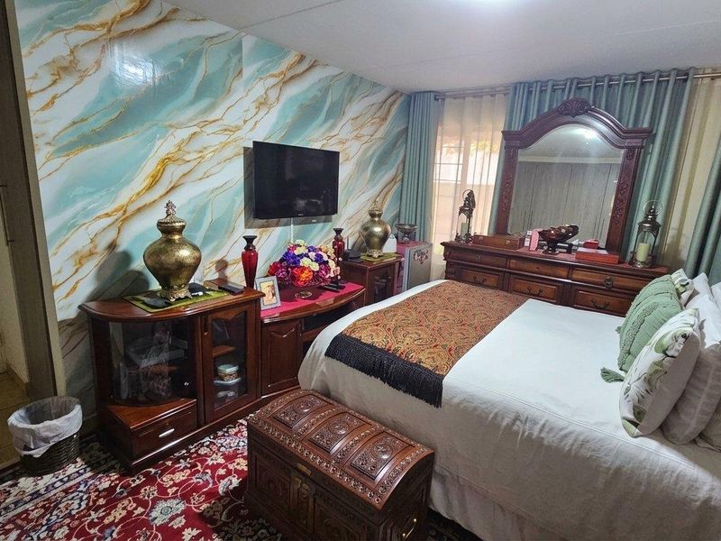 A bedroom featuring decorative marble-effect wall paneling and a wall-mounted television.