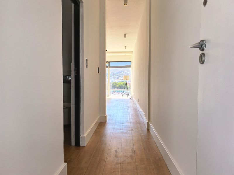 A bright, clean hallway with light wood-look laminate flooring leading towards an open living area with natural light.