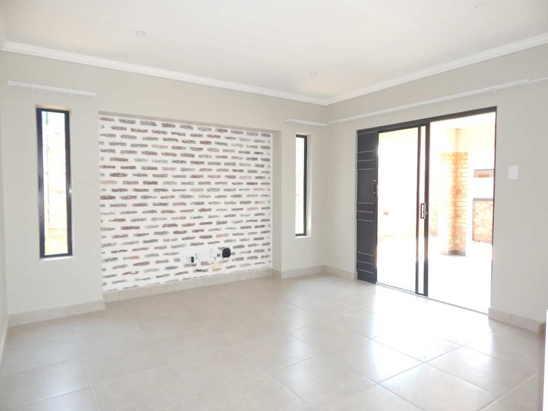 A bright, empty living room featuring a decorative exposed brick wall, neutral tiled flooring, and sliding glass doors leading to an outdoor patio area.