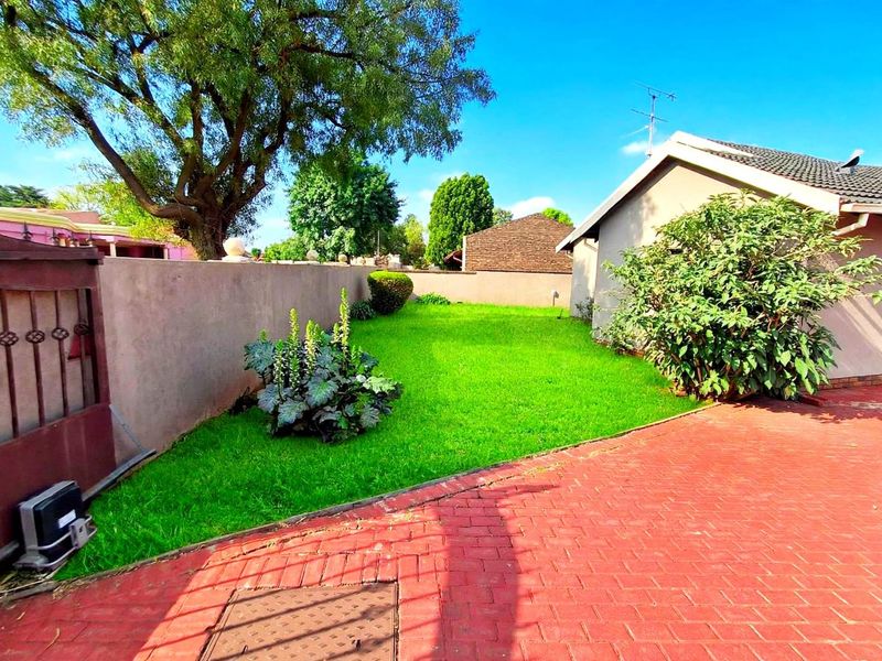 A private rear garden area featuring a well-maintained lawn, paved driveway, and secure boundary walling.