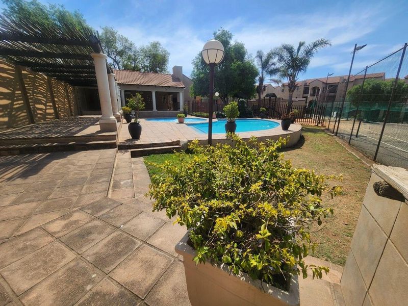 Communal outdoor area featuring a swimming pool, paved patio space, pergola, and adjacent tennis court facilities.