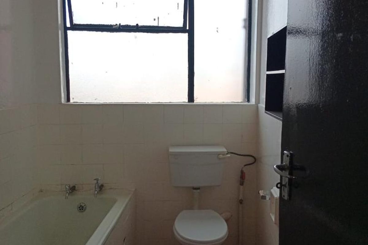 A dated bathroom featuring a standard bathtub, toilet, and tiled finishes, requiring cosmetic updates to modernize the space.