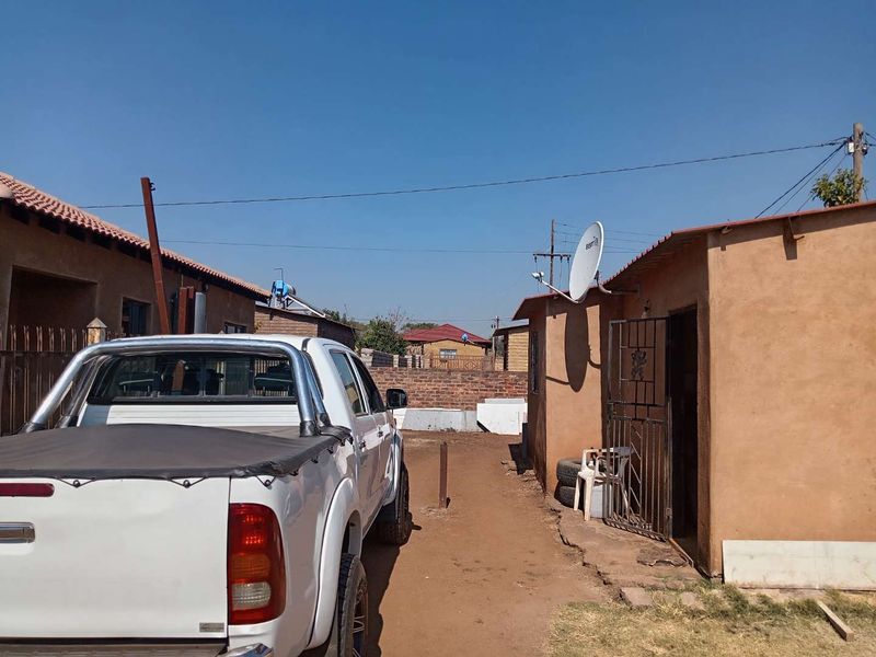 Rear exterior view of the property showing a side pathway, brick boundary wall, and basic building structure with a satellite dish.