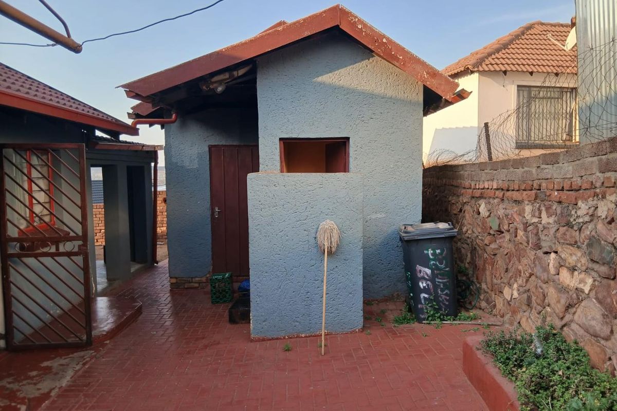 Rear exterior view of the property featuring a small outbuilding, brick paved courtyard, and stone boundary wall.