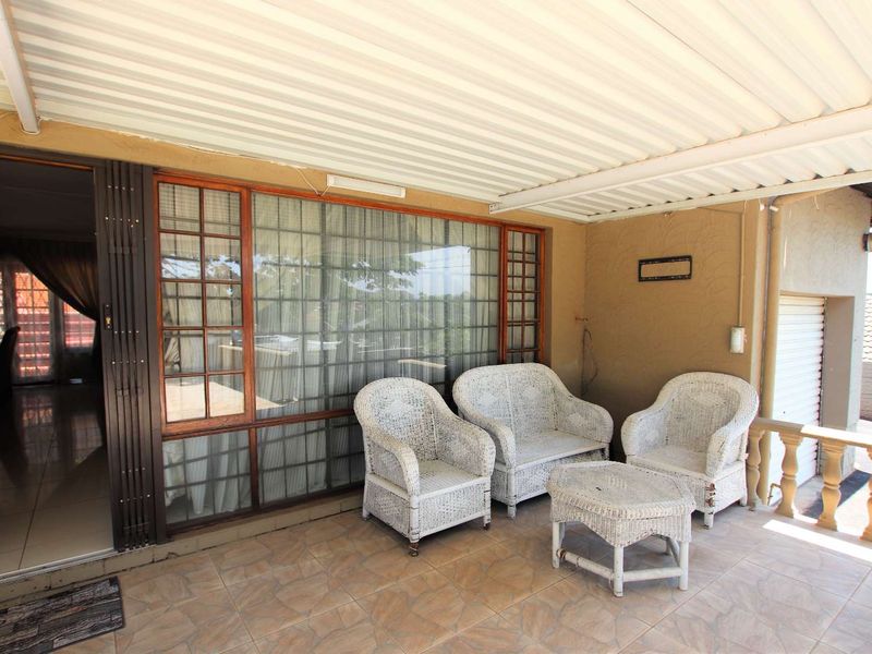 A covered patio area featuring tiled flooring, a corrugated metal roof, and access to the interior through a sliding glass door.