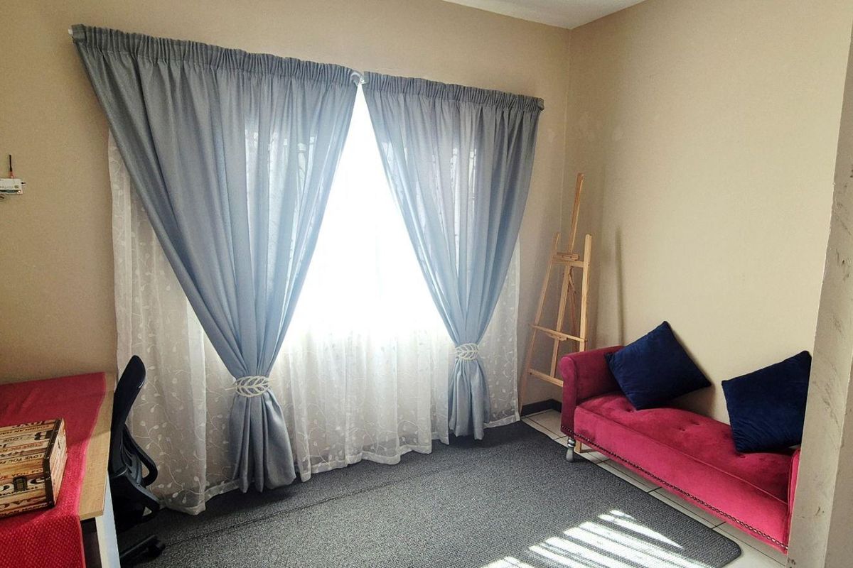 A functional bedroom space featuring neutral wall tones, tiled flooring, and a window dressed with curtains.