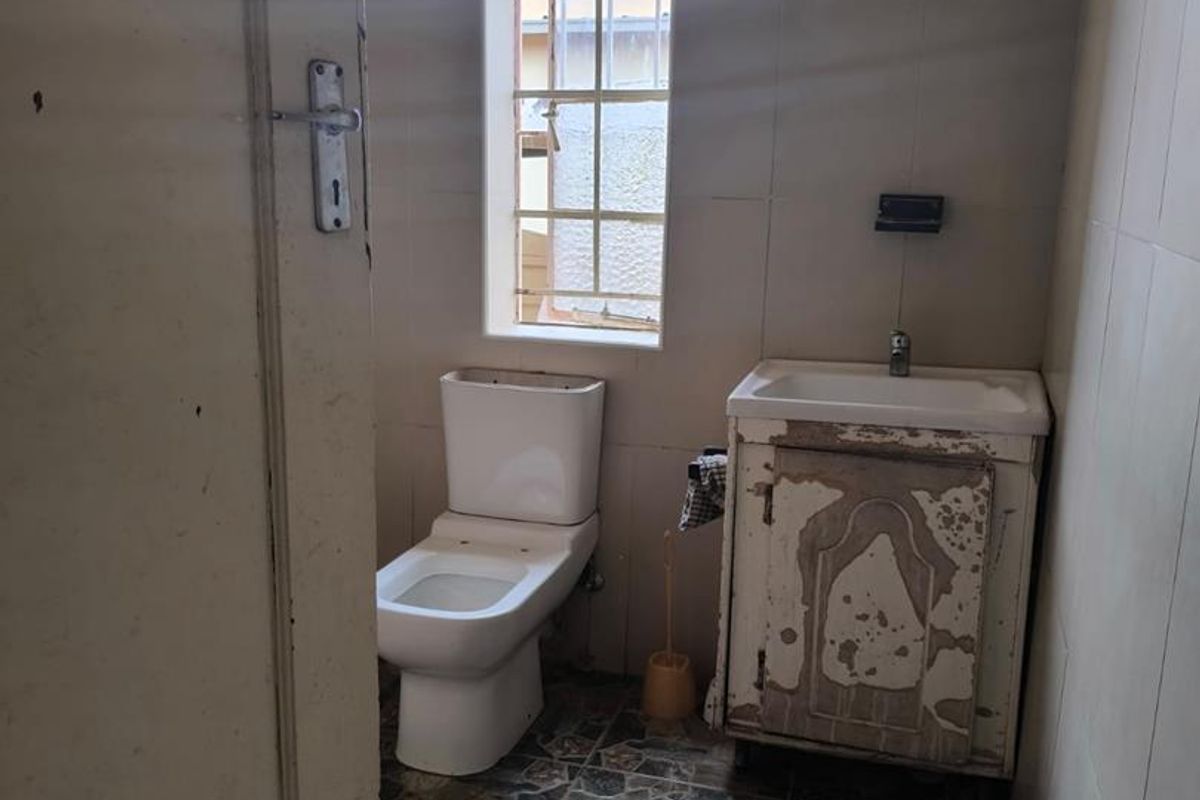 A small, dated bathroom featuring a toilet and a vanity unit with a basin, requiring cosmetic updates and refurbishment.