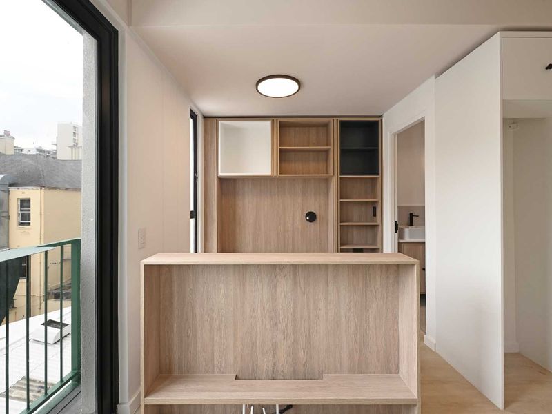 A modern, minimalist living area featuring light wood built-in cabinetry, integrated shelving, and direct access to a private balcony.