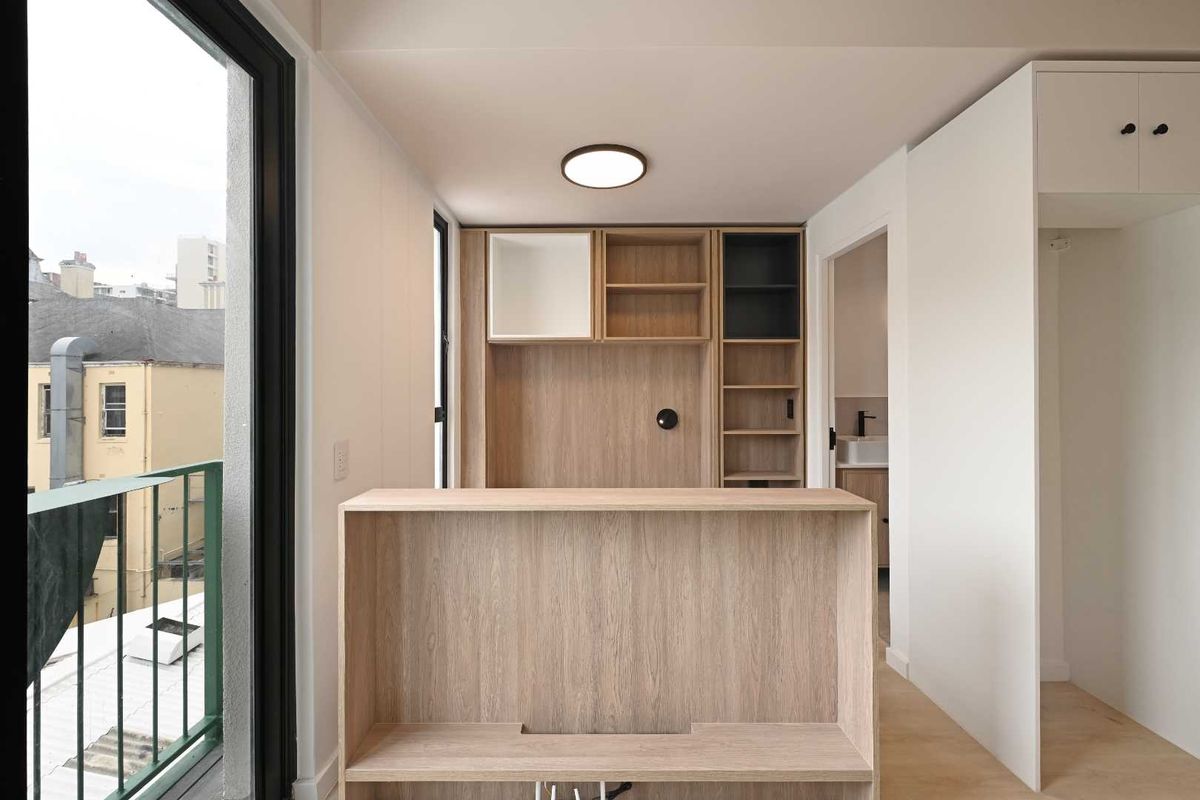 A modern, minimalist living area featuring light wood built-in cabinetry, integrated shelving, and direct access to a private balcony.