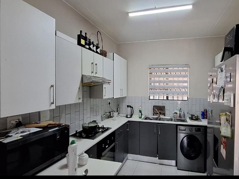 A functional kitchen featuring modern two-tone cabinetry, a gas hob, built-in oven, and integrated laundry plumbing with a tiled backsplash.