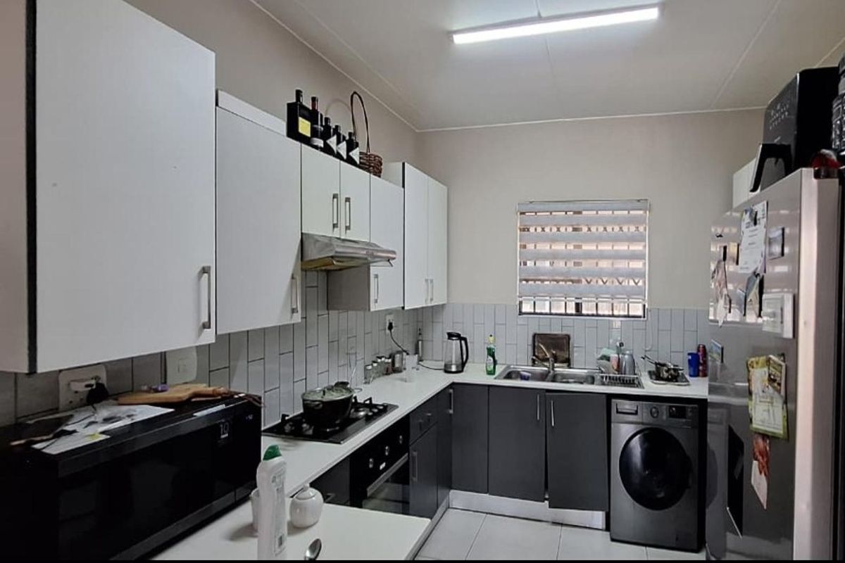 A functional kitchen featuring modern two-tone cabinetry, a gas hob, built-in oven, and integrated laundry plumbing with a tiled backsplash.