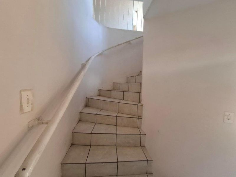 A simple interior staircase featuring tiled steps and a white handrail, providing access between levels in the apartment.