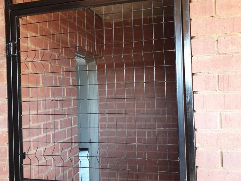 A secure metal gate entrance featuring exposed brick walls and a concrete ceiling, providing a functional and secure access point to the apartment.