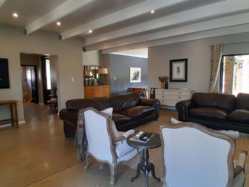 Spacious open-plan living area featuring exposed ceiling beams, recessed lighting, and polished concrete floors with direct access to the outdoor patio.