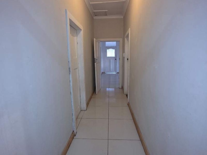 A simple, empty hallway featuring white tiled flooring, neutral walls, and standard door frames leading to adjacent rooms.