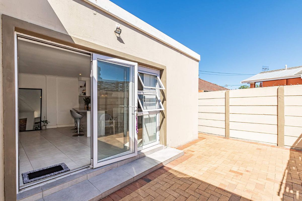 Exterior view of a paved rear courtyard featuring a modern sliding glass door entrance leading into an open-plan living space.