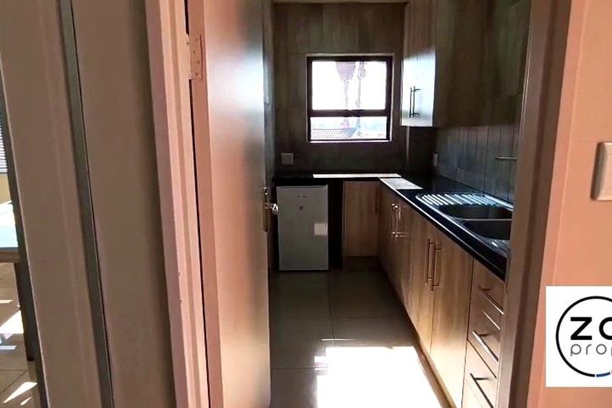 A compact, functional kitchen featuring modern wood-finish cabinetry, dark countertops, and a tiled backsplash, providing efficient workspace for an office environment.