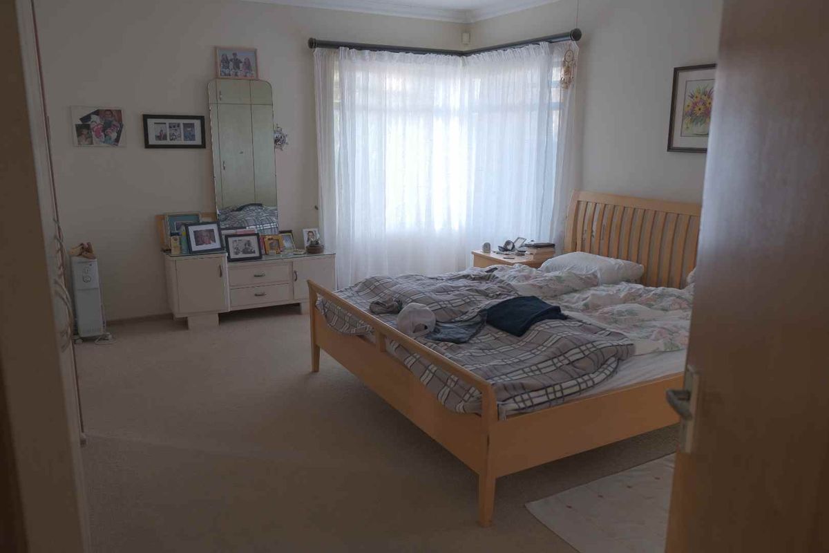 A spacious bedroom featuring neutral carpeting, a large bay window with sheer curtains, and coved ceiling detailing.