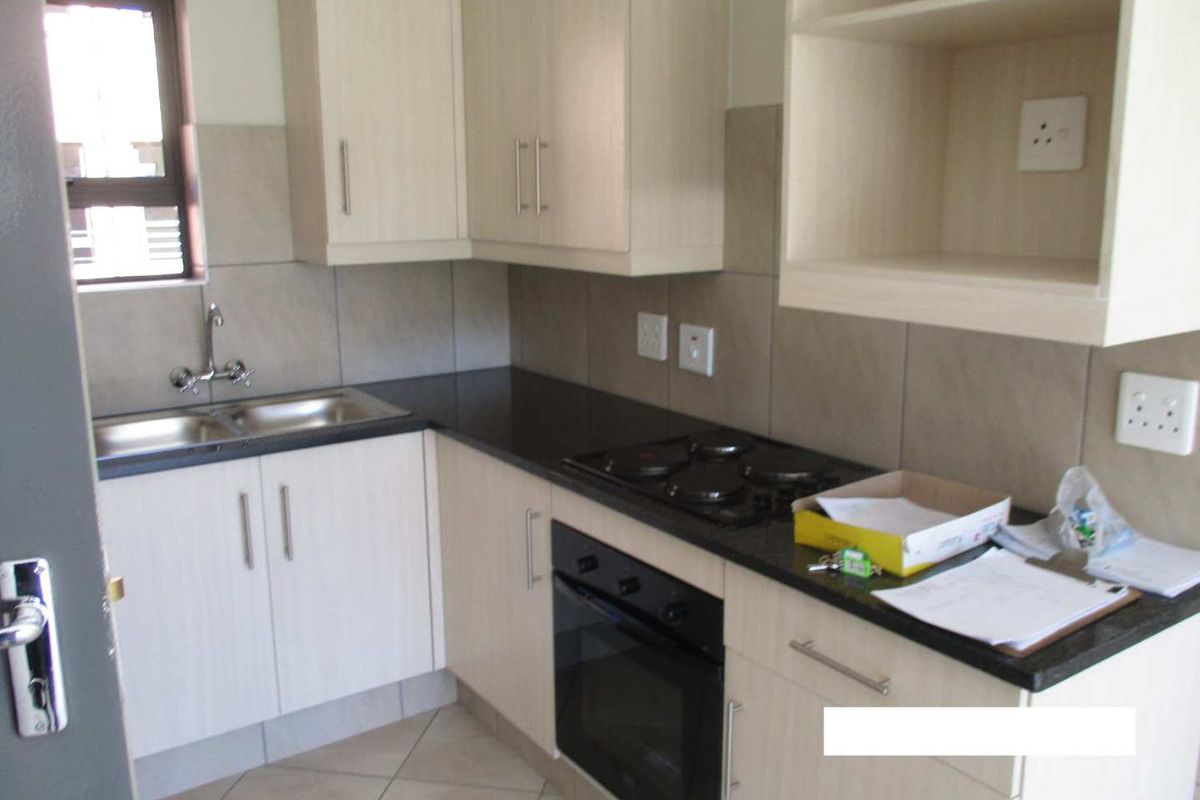 A clean, functional kitchen featuring light wood-finish cabinetry, black granite countertops, a built-in oven, electric hob, and a double sink with tiled backsplash.
