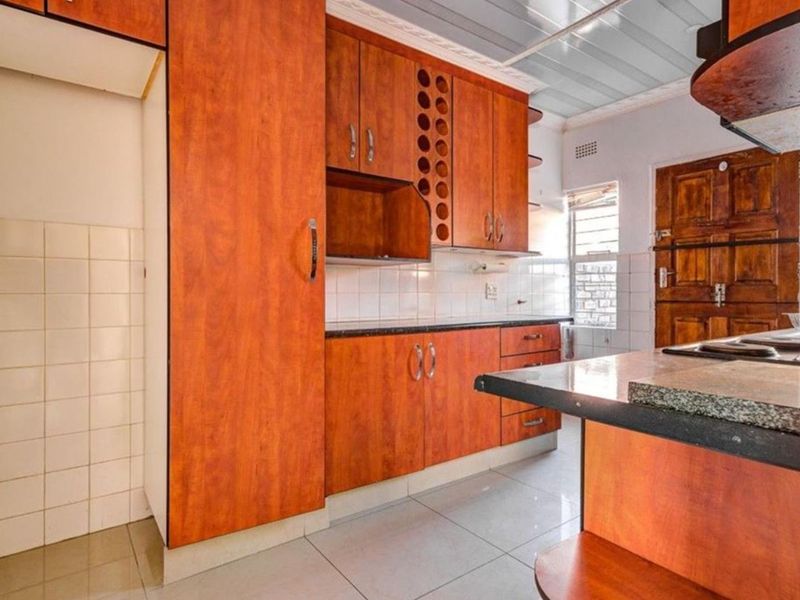 A functional kitchen featuring wood-finish cabinetry, granite countertops, tiled backsplash, and tiled flooring, offering a classic layout ready for modernization.