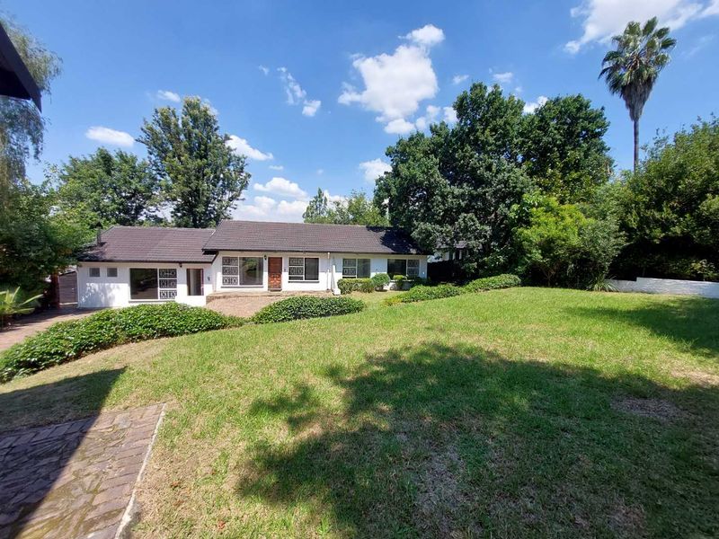 Rear view of the house featuring a tiled roof, security-barred windows, a paved patio area, and a spacious established garden with mature trees.