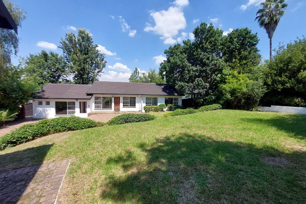 Rear view of the house featuring a tiled roof, security-barred windows, a paved patio area, and a spacious established garden with mature trees.