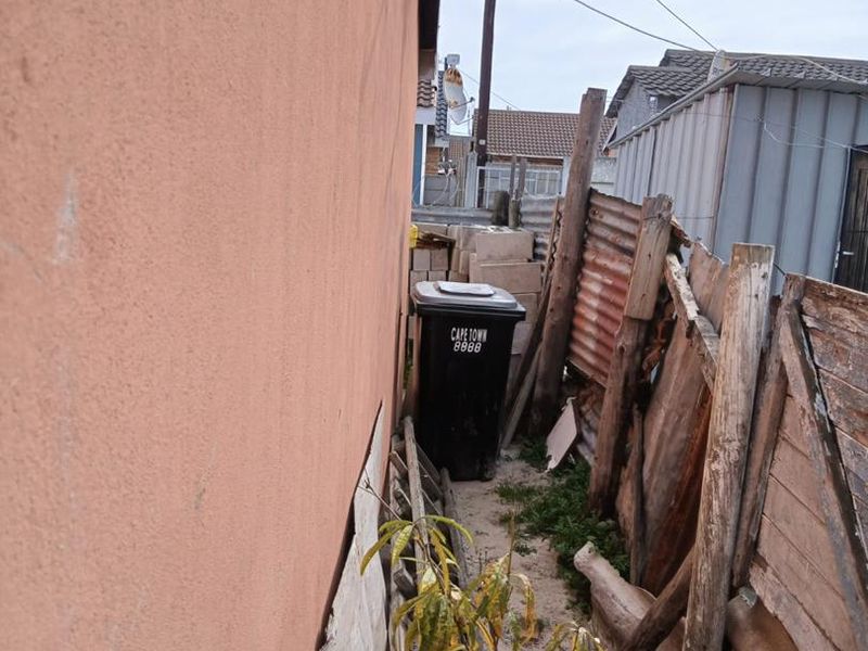 A narrow side passage of the property featuring a satellite dish mounted on the exterior wall and weathered corrugated metal fencing.