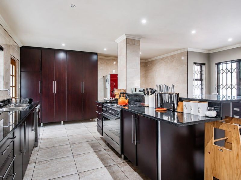 Spacious kitchen featuring dark wood cabinetry, granite countertops, a stainless steel gas stove, and tiled flooring with ample storage space.