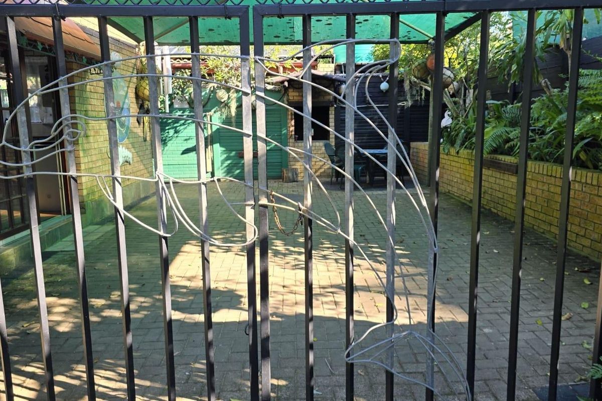 A view through a decorative metal gate into a paved courtyard area with brick walls and a covered outdoor space.