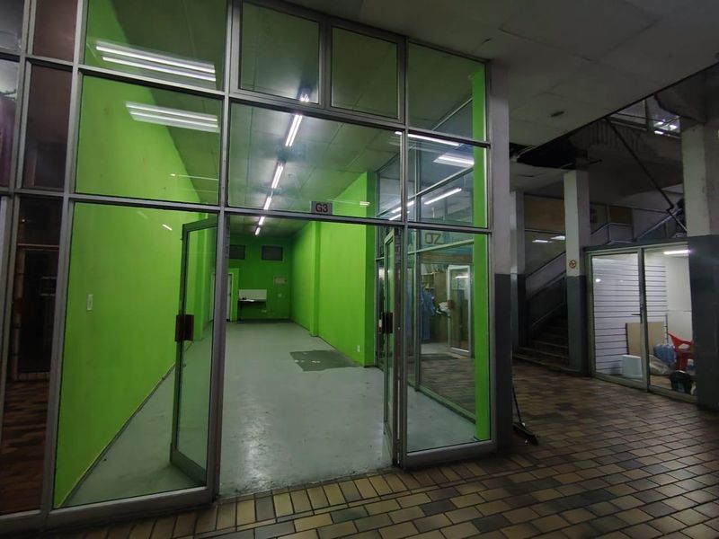 Vacant retail unit featuring a glass storefront, fluorescent lighting, and tiled flooring, located within a commercial building complex.