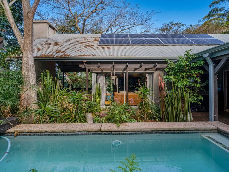 Outdoor pool area featuring a swimming pool, timber pergola, and a corrugated metal roof equipped with solar panels.