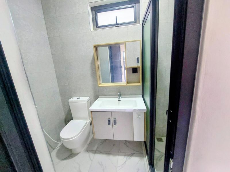 A modern bathroom featuring a wall-mounted vanity with integrated sink, a toilet, and a glass-enclosed shower area with neutral wall tiling.