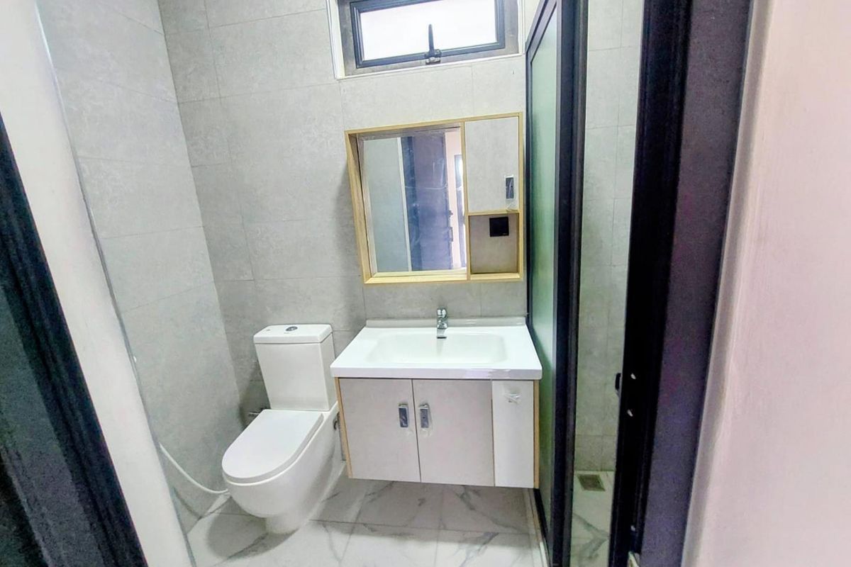 A modern bathroom featuring a wall-mounted vanity with integrated sink, a toilet, and a glass-enclosed shower area with neutral wall tiling.