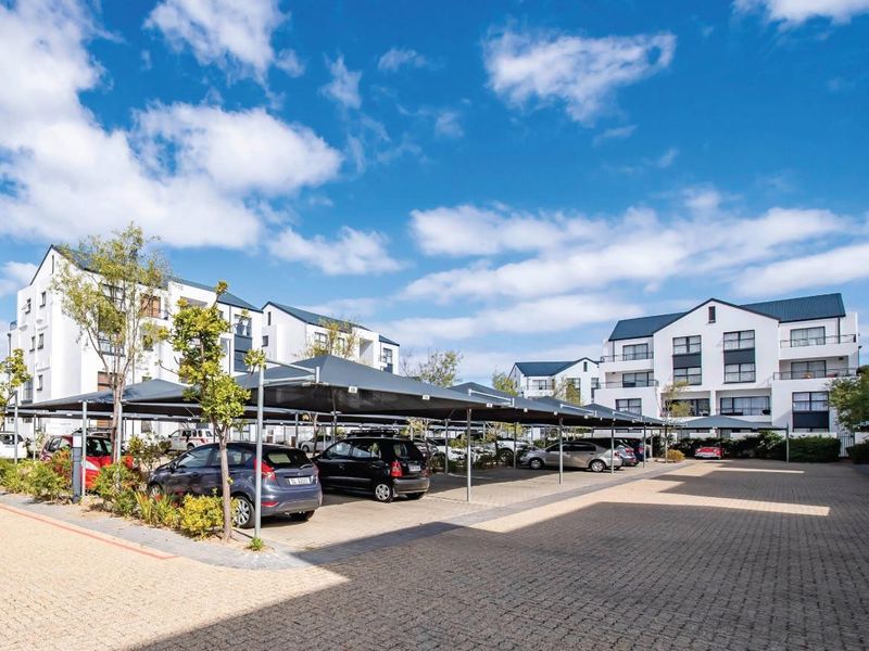 Exterior view of a modern apartment complex featuring paved parking areas with shade cloth carports and well-maintained multi-story residential buildings.