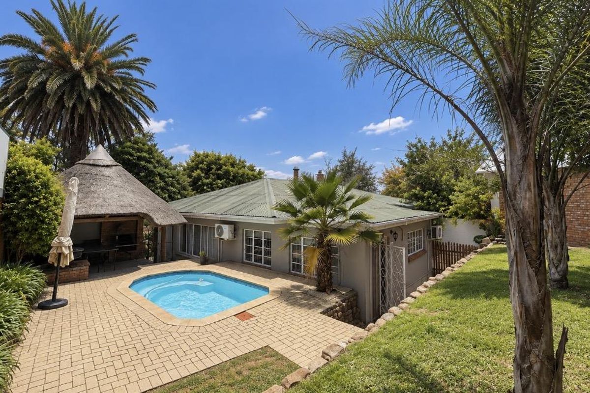 Rear garden area featuring a swimming pool, paved patio, and a traditional thatched lapa, ideal for outdoor entertaining.