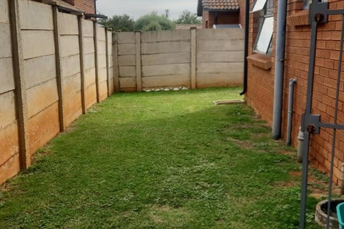 A private side garden area featuring a brick exterior wall, precast concrete boundary fencing, and a grass lawn.