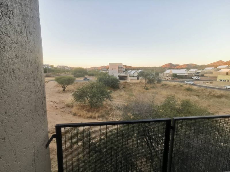 An elevated view from a balcony overlooking a dry landscape with surrounding residential properties and distant hills.