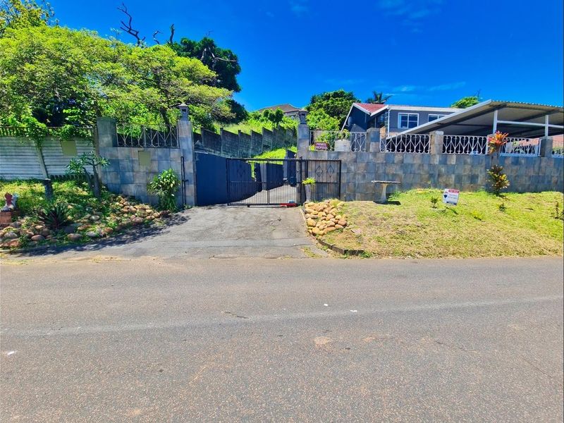 Front view of the property featuring a stone-clad boundary wall, secure metal driveway gate, and an attached carport.