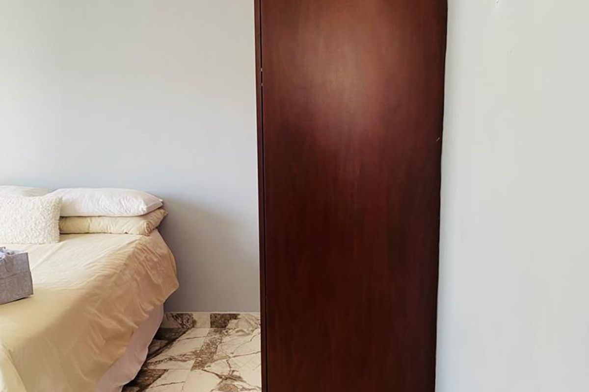 A bedroom featuring marble-look floor tiles and a dark wood built-in wardrobe.