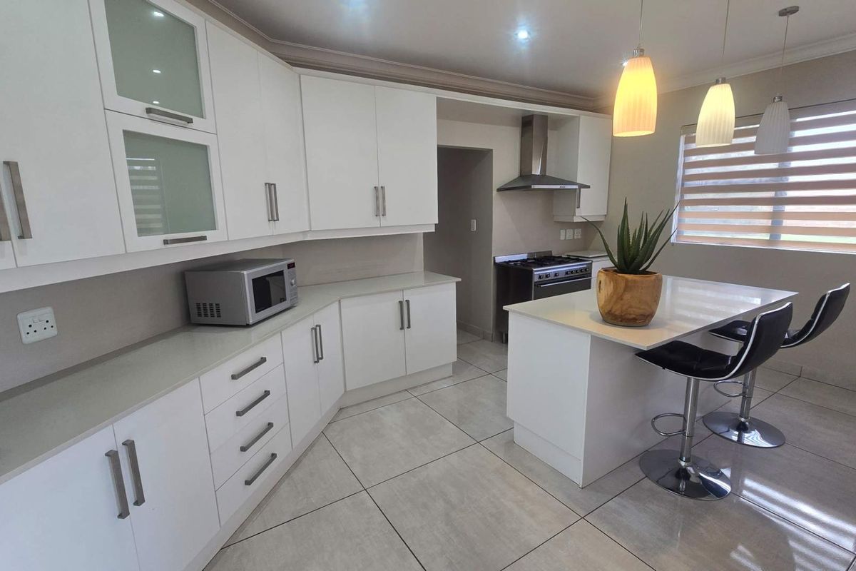 Modern kitchen featuring white cabinetry, stone countertops, a central island with breakfast bar seating, and a stainless steel extractor fan.