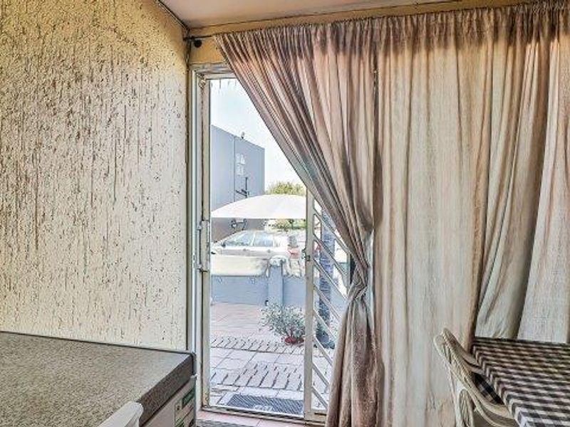 A covered patio area featuring a sliding glass door with security gate and textured wall finish, providing access to the exterior space.