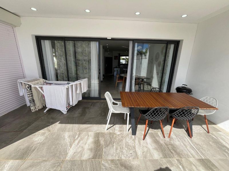 A covered patio area featuring large format floor tiles, recessed lighting, and wide sliding glass doors providing seamless access to the interior living space.