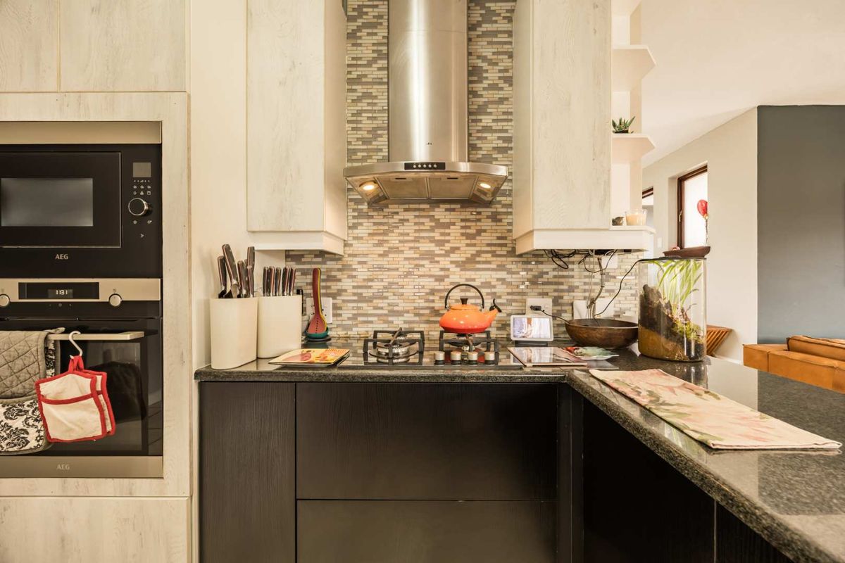 Modern kitchen featuring built-in AEG appliances, granite countertops, a mosaic tile backsplash, and a stainless steel extractor fan.