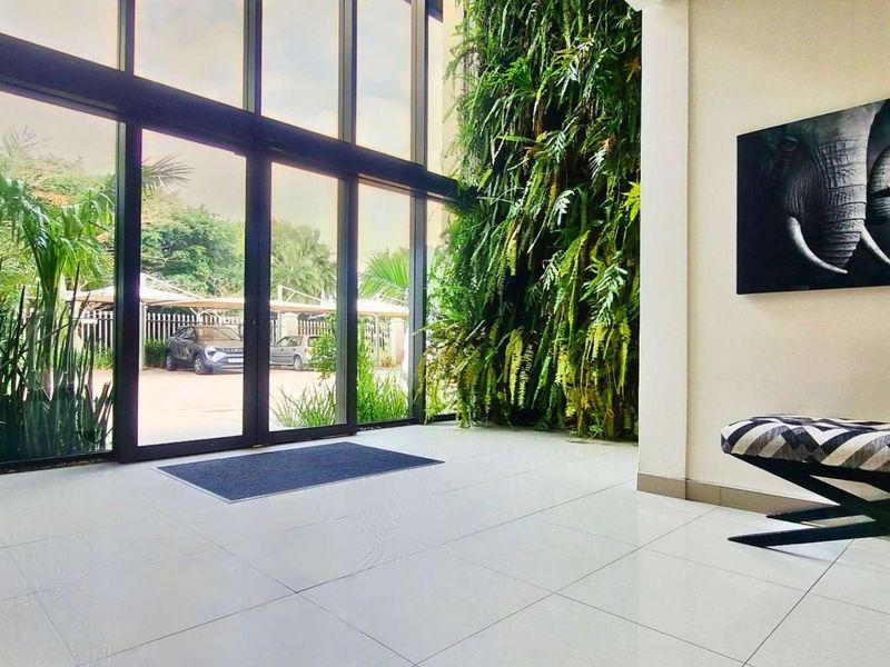 Modern office entrance lobby featuring floor-to-ceiling glass windows, a striking vertical garden wall, and polished tiled flooring.
