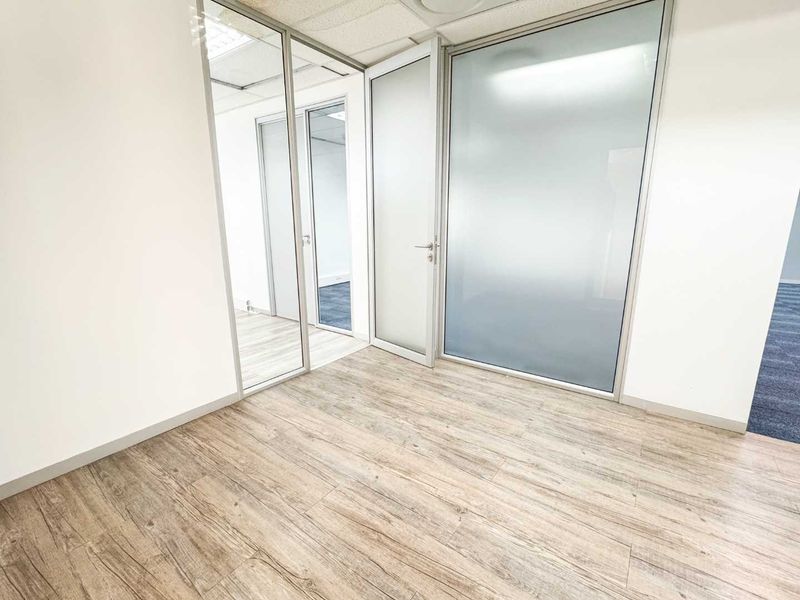 A bright, modern office space featuring wood-look laminate flooring and professional aluminium-framed glass partitions with frosted privacy panels.